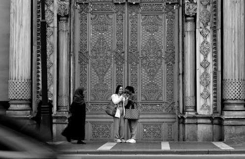 A black and white photo of two people standing in front of a large ornate door