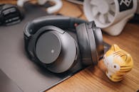 木制桌子上，时尚的无线耳机旁摆放着一座可爱的猫雕像，堪称技术爱好者的完美搭配