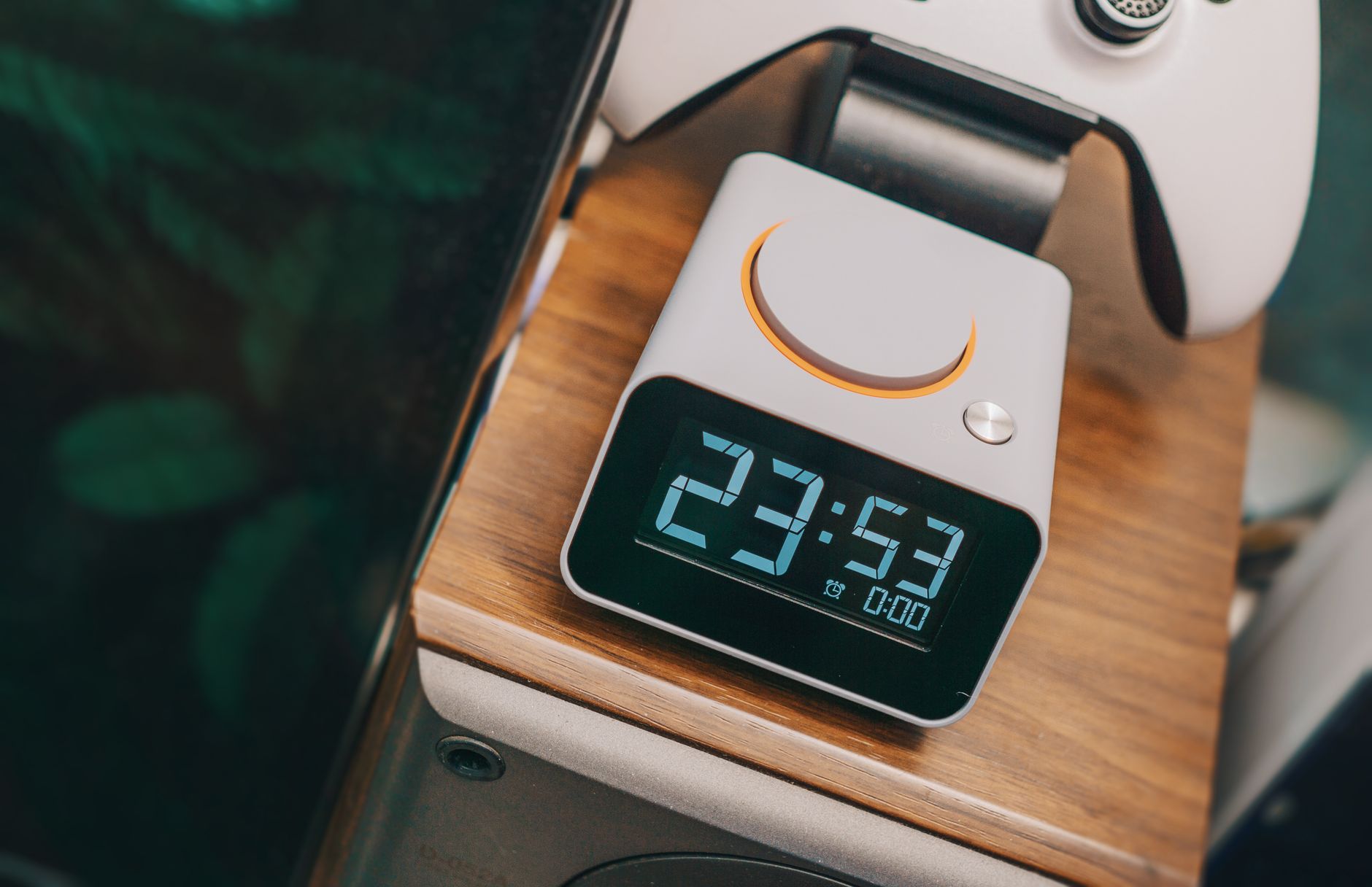 Close-up of a sleek digital clock displaying time, set on a contemporary wooden surface near electronics.