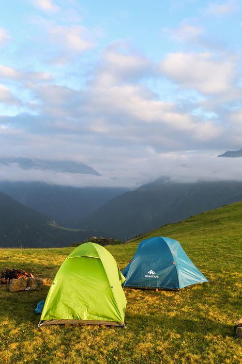 Free Two colorful tents pitched in a scenic mountain valley under a cloudy blue sky. Stock Photo