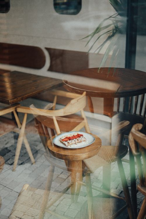 Free Warm café setting showcasing a plate of dessert on a wooden table through a window. Stock Photo