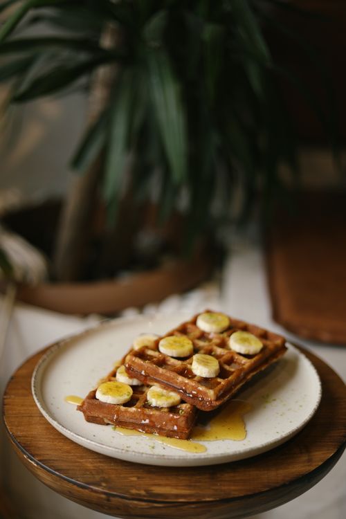 Free Tasty waffles topped with banana slices and syrup on a rustic plate, perfect for breakfast. Stock Photo