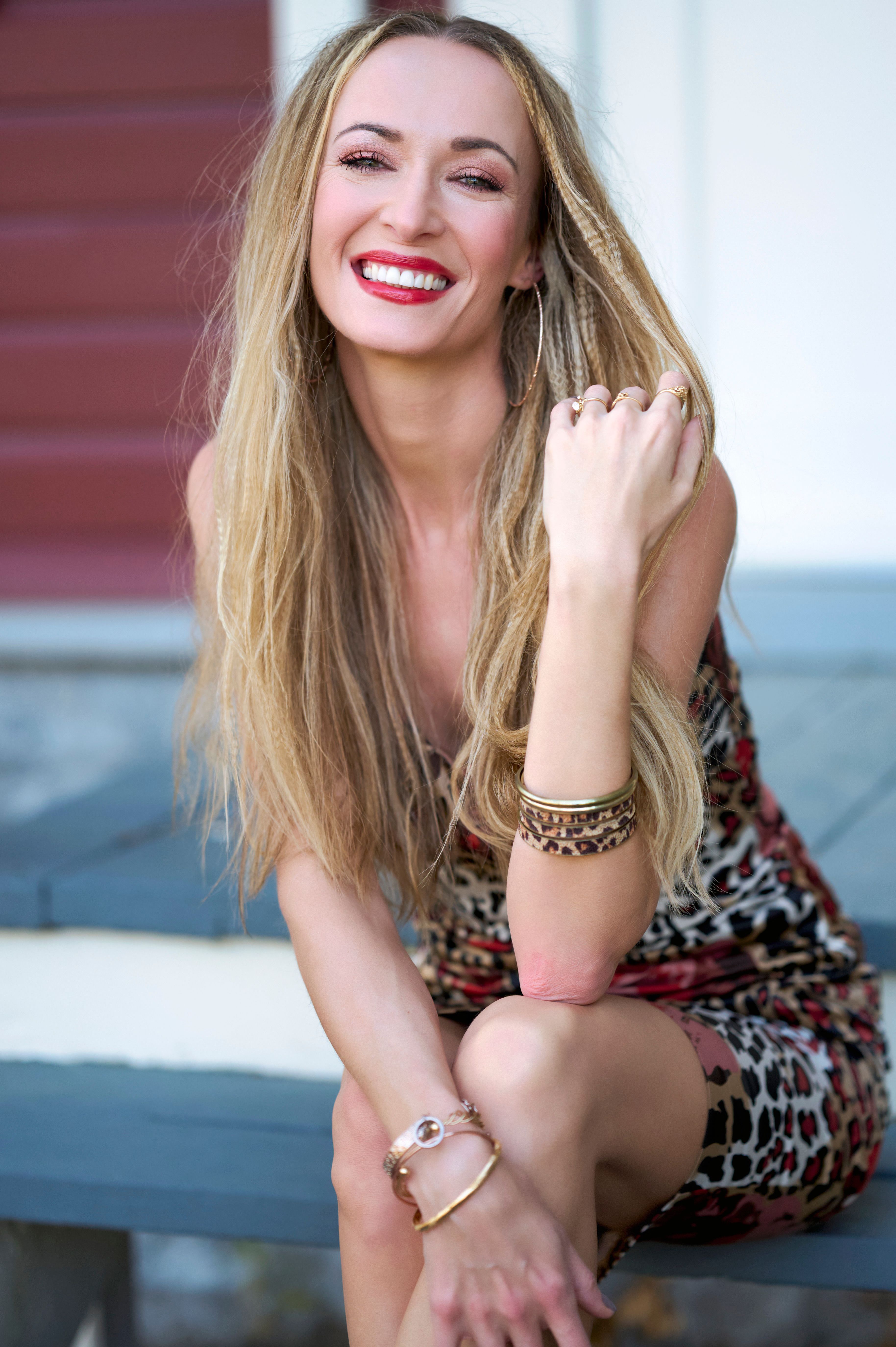 A joyful woman with long blonde hair sitting outdoors in a leopard print dress.