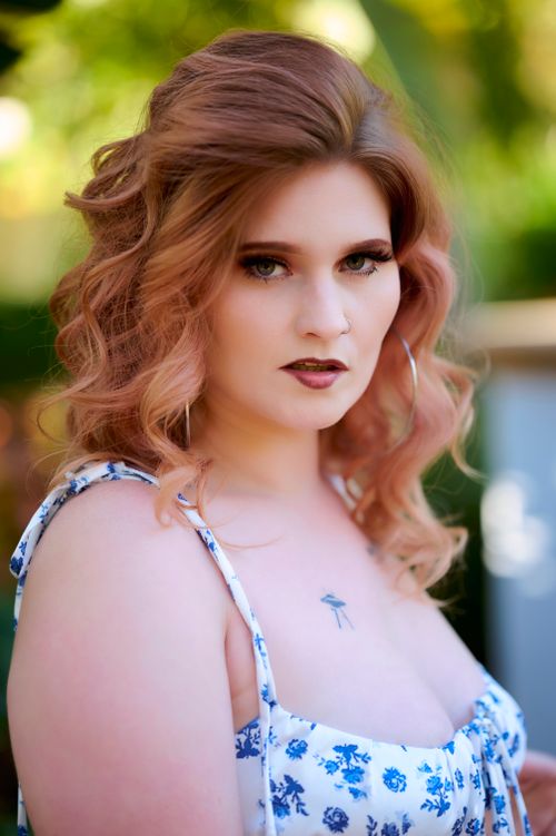 Free Portrait of a woman with curled hair and distinct makeup in a floral dress outdoors. Stock Photo