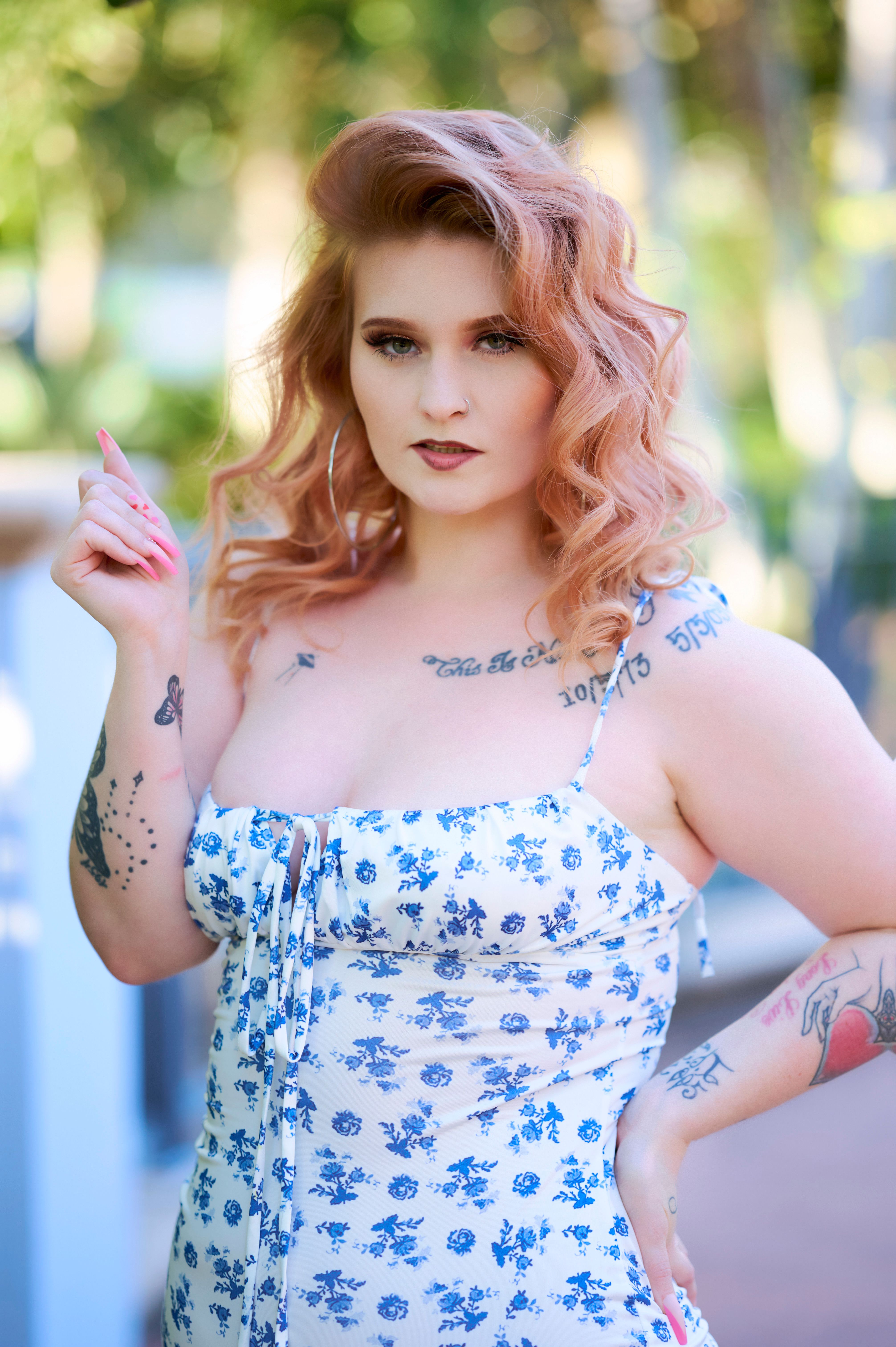Chic young woman with tattoos posing in a floral dress outdoors.