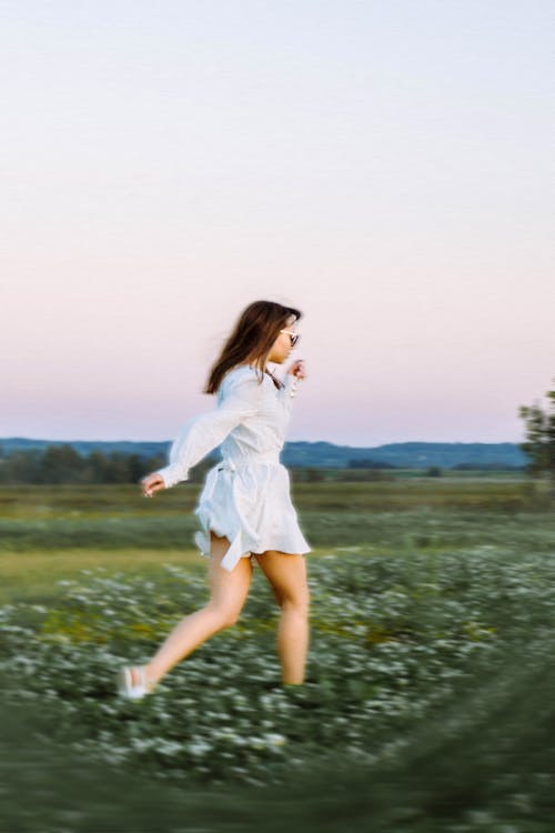 young beautiful girl in a white short dress running through a field at sunset 