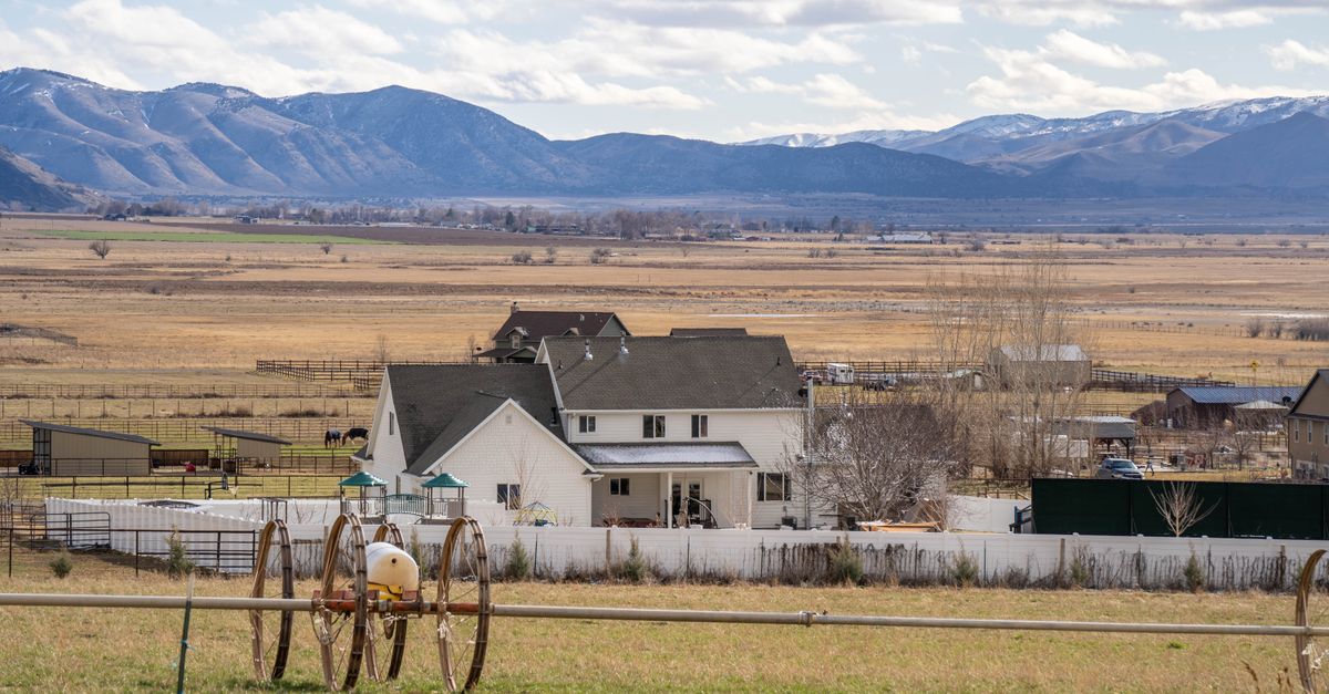 Rustic farmhouse in a rural landscape with mountains and fields in the background, ideal for countryside living.