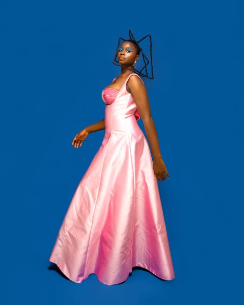 Free Stylish black woman wearing a pink gown and unique headpiece against a blue background. Stock Photo