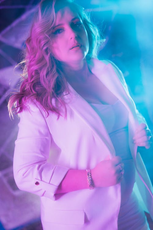 A woman in a white suit posing in front of a neon light