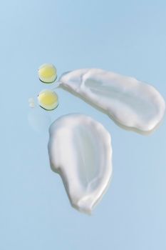 Close-up of skincare cream and oil drops on a blue surface.