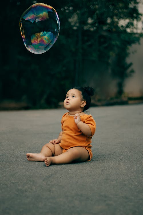 A baby sitting on the ground with a bubble