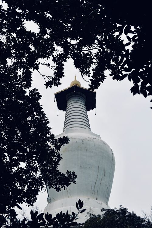 Free A serene view of a white pagoda in Suzhou, China, framed by leafy tree branches. Stock Photo