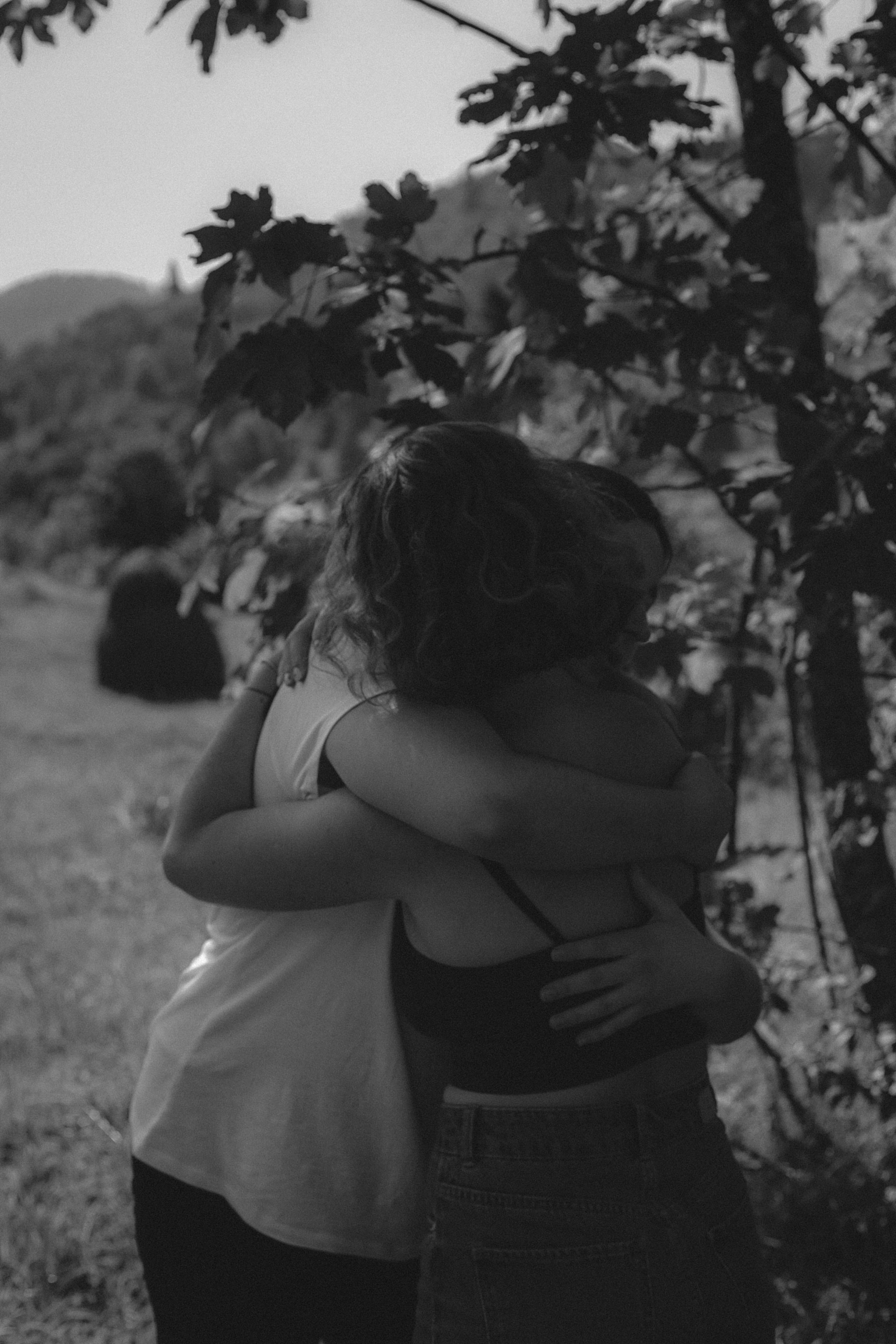 Two people warmly embracing outdoors in a scenic rural setting.