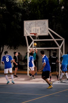 Men playing a competitive basketball game on an outdoor court surrounded by trees.