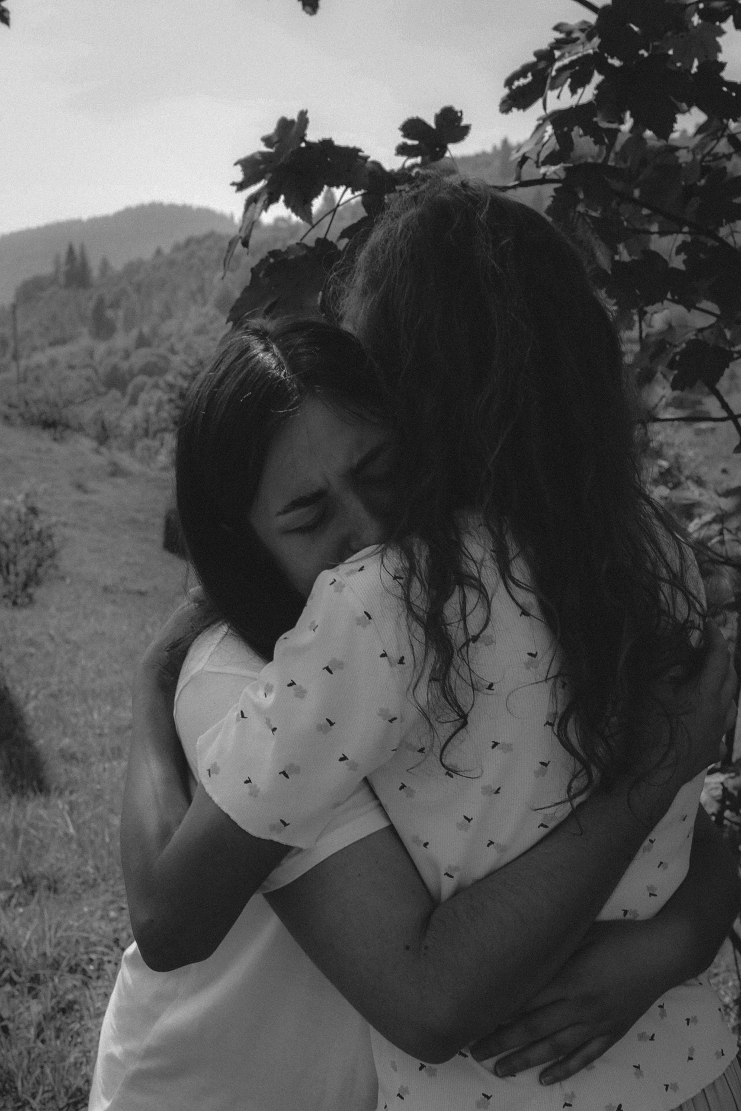 Two women share a heartfelt embrace in a serene outdoor setting.