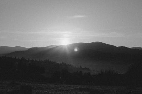 Black and white photo of sun rising over mountains