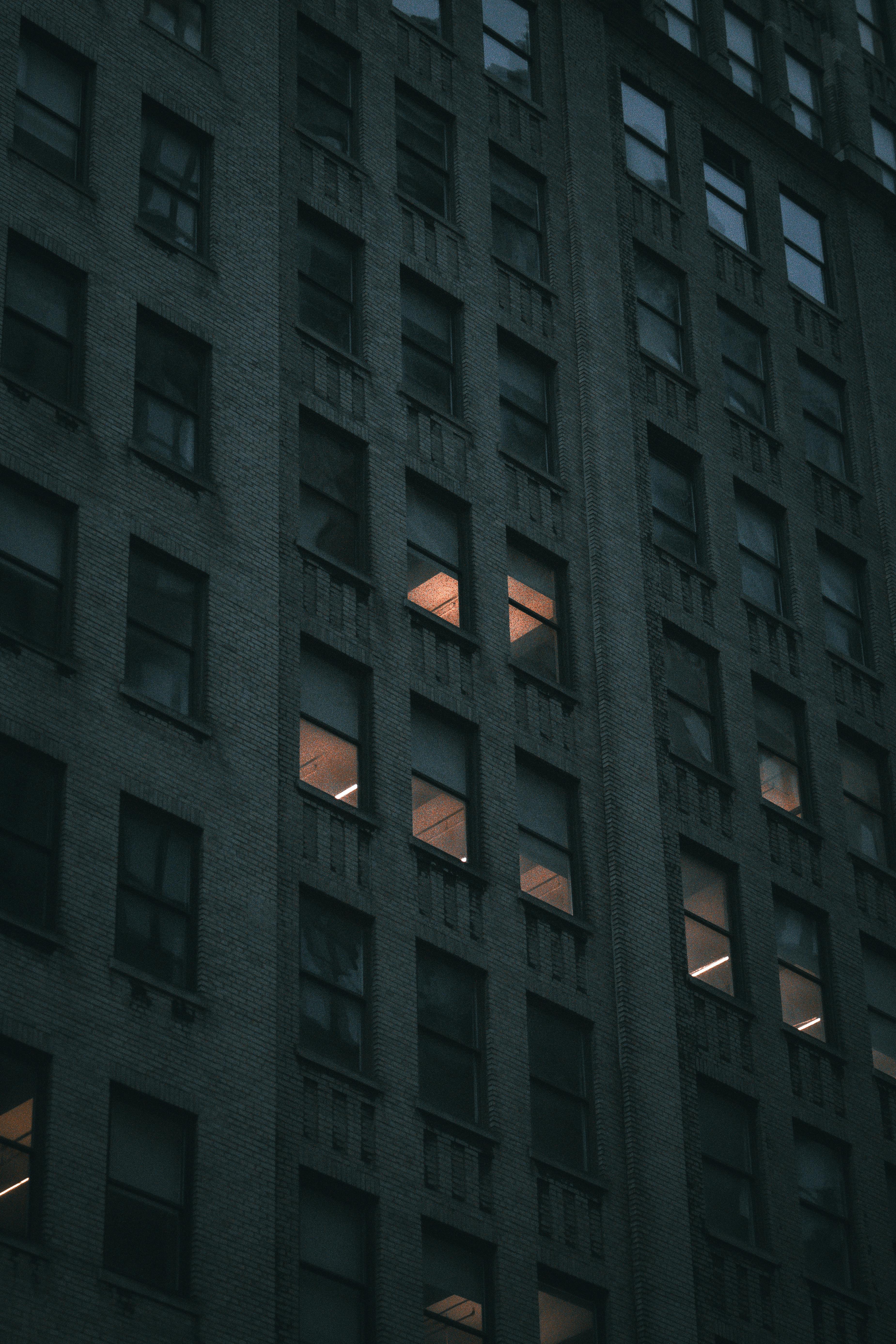 Dark and atmospheric view of a New York City skyscraper with illuminated windows at night.
