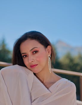 Portrait of a woman with elegant earrings and makeup, posing against a scenic outdoor backdrop.