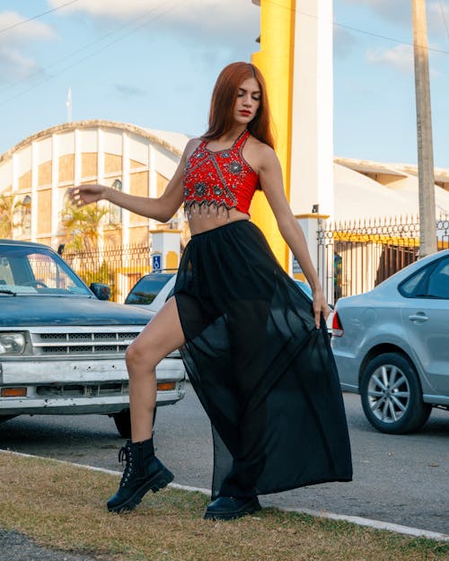 A woman in a red top and black skirt standing in front of a car