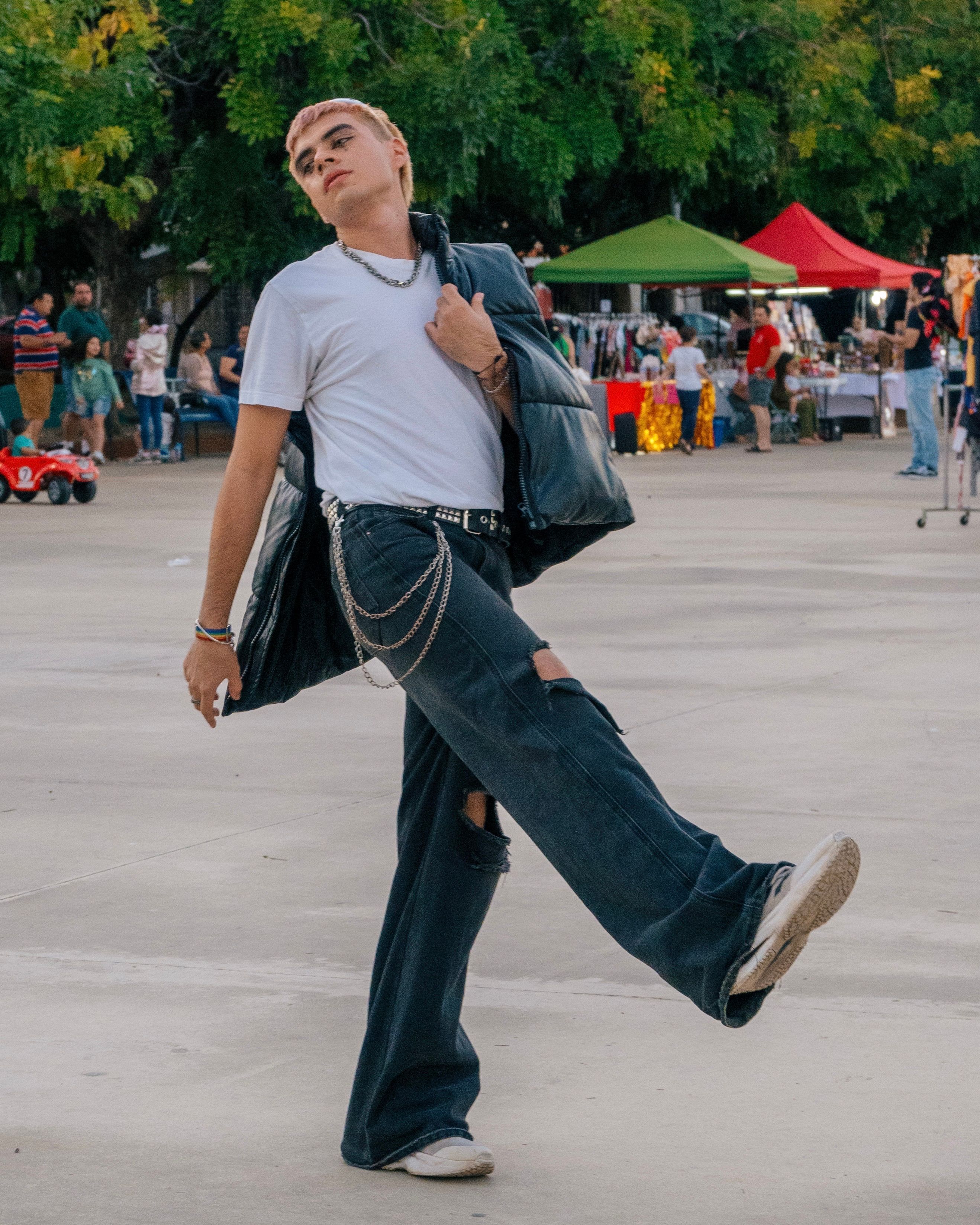 A young man in casual attire poses confidently on a bustling urban street during the day.