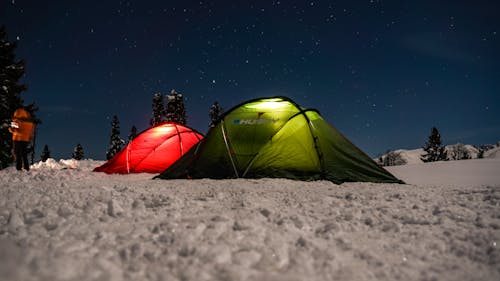 Two tents are set up in the snow at night