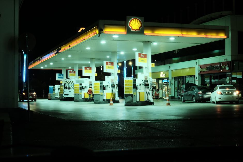 Nighttime view of an illuminated Shell gas station with cars parked and filling up.