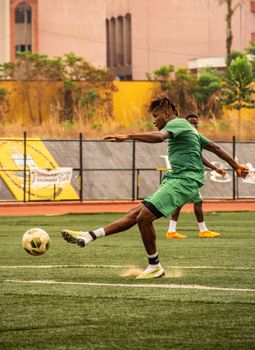 African male soccer player kicking the ball on a field in full action.