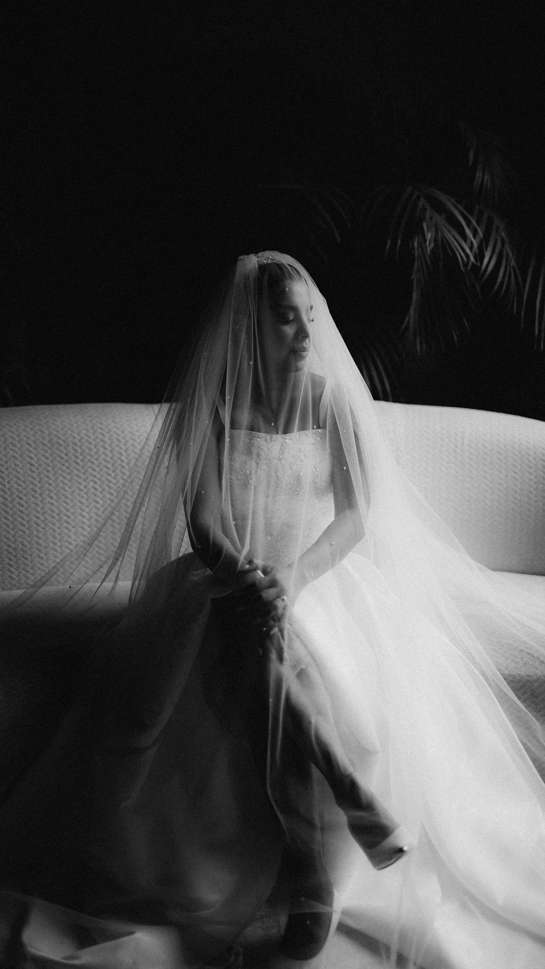 A striking black and white portrait of a bride in a wedding dress sitting gracefully.