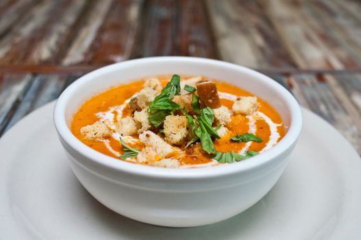 A gourmet bowl of creamy tomato soup garnished with croutons and fresh herbs, perfect for a cozy meal.