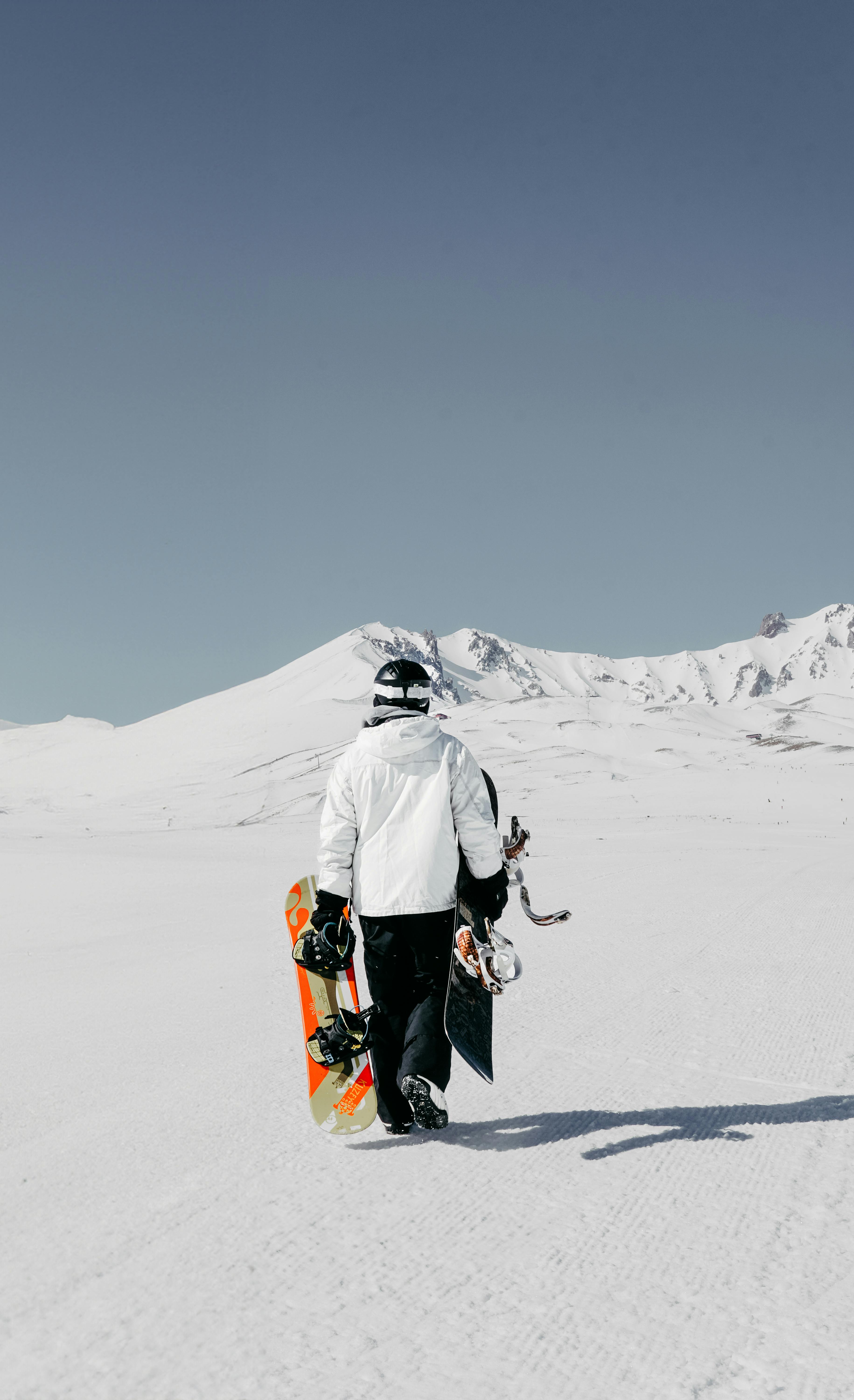 Person walking with snowboard in snowy mountain scene, perfect for winter sports enthusiasts.