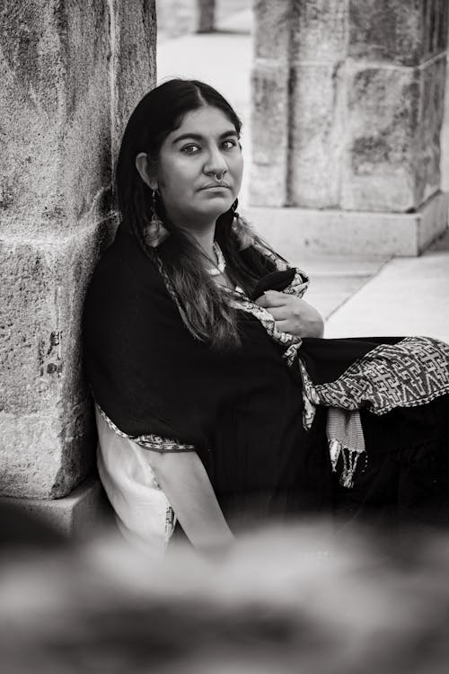 Woman in Poncho Sitting by Wall in Black and White