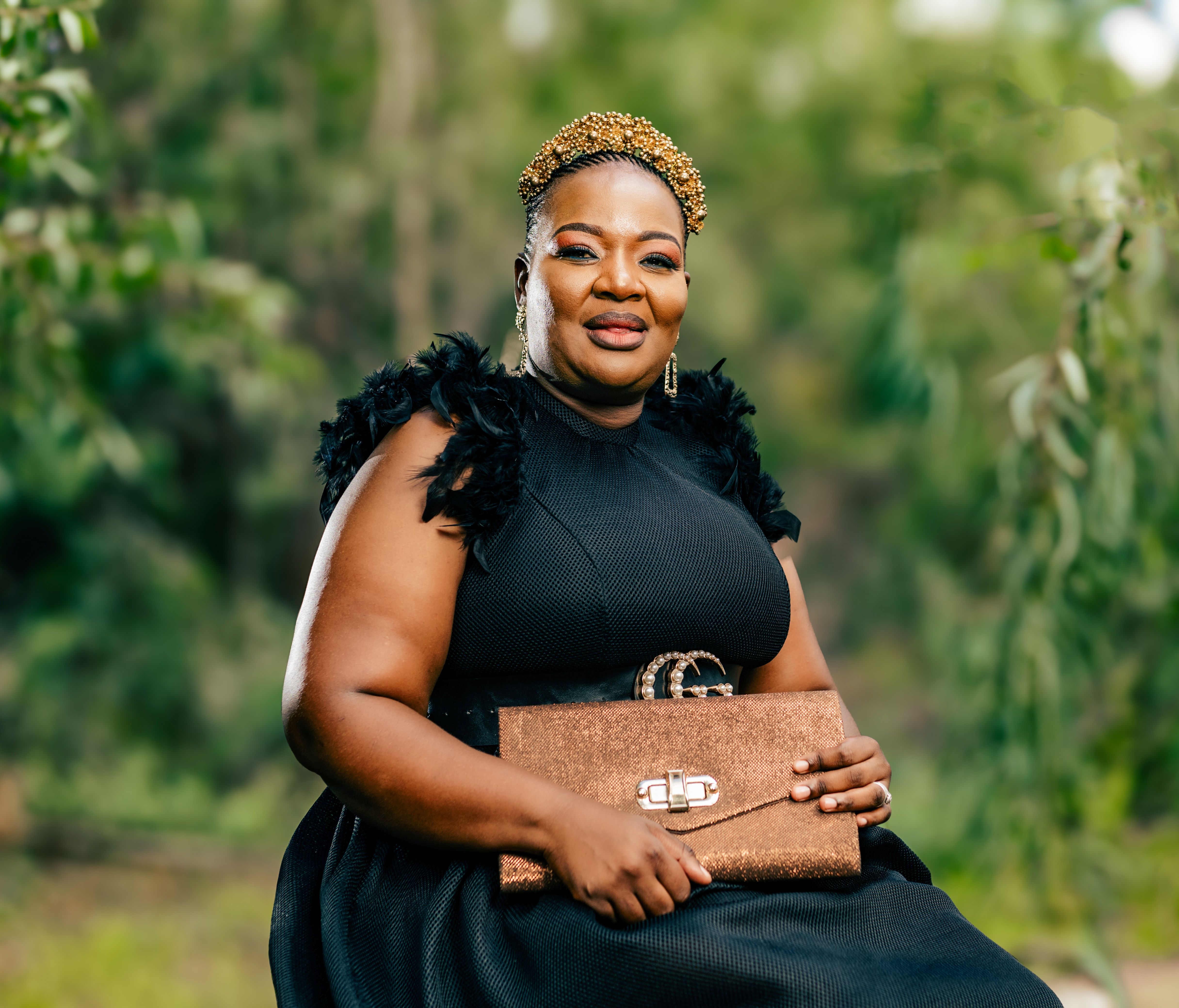 Portrait of a fashionable woman in a black dress outdoors, holding a stylish clutch and wearing a decorative crown.