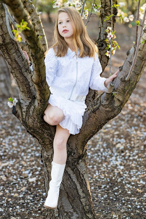 Free A Little Girl in White Clothing Sitting on a Tree Stock Photo