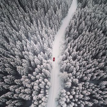 Stunning aerial shot of a red car on a snow-covered road, Norway winter forest.