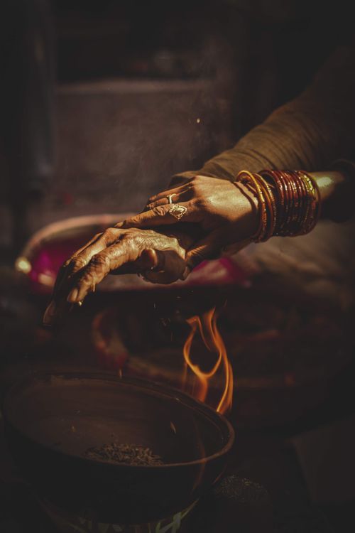 Free A woman's hand adorned with bangles reaches over a flame, creating a warm, atmospheric scene. Stock Photo