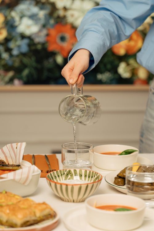 Free Close-up of a hand pouring water into a glass surrounded by dishes on a dining table. Stock Photo