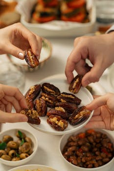 Hands reaching for stuffed dates at an iftar table with olives and beans.