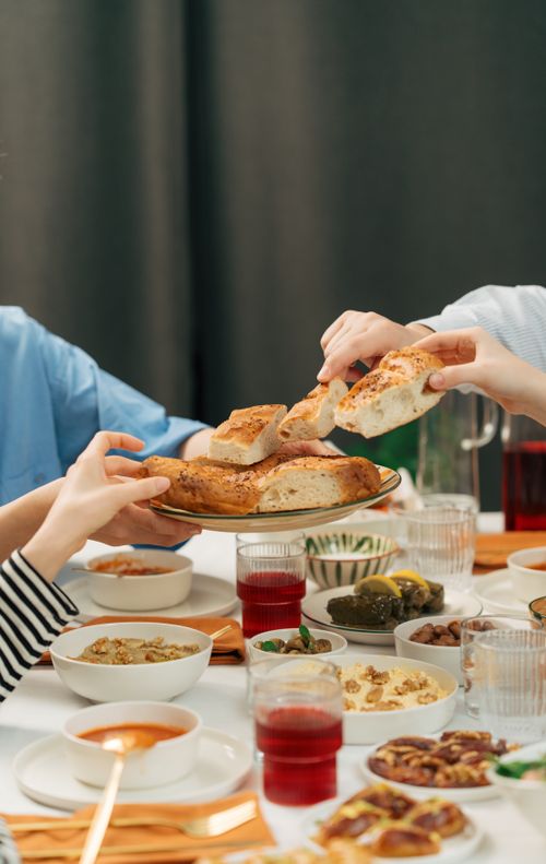 Free People sharing bread at a vibrant dinner table, featuring diverse dishes and drinks, creating a warm atmosphere. Stock Photo