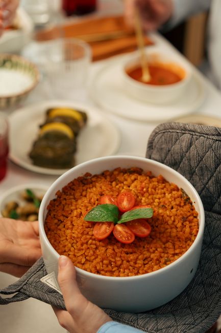 A bowl of cooked bulgur wheat with separate, fluffy tan grains, garnished with parsley and a wedge of lemon on the side.