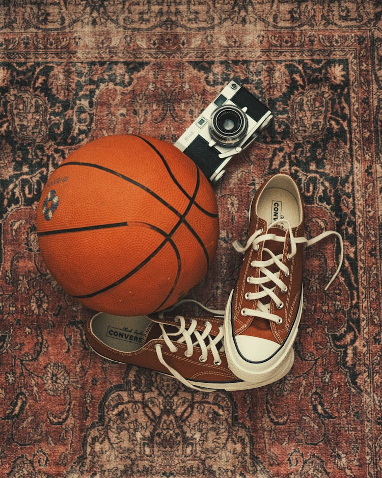 Sneakers, A Basketball And An Analog Camera Lying On An Old Rug