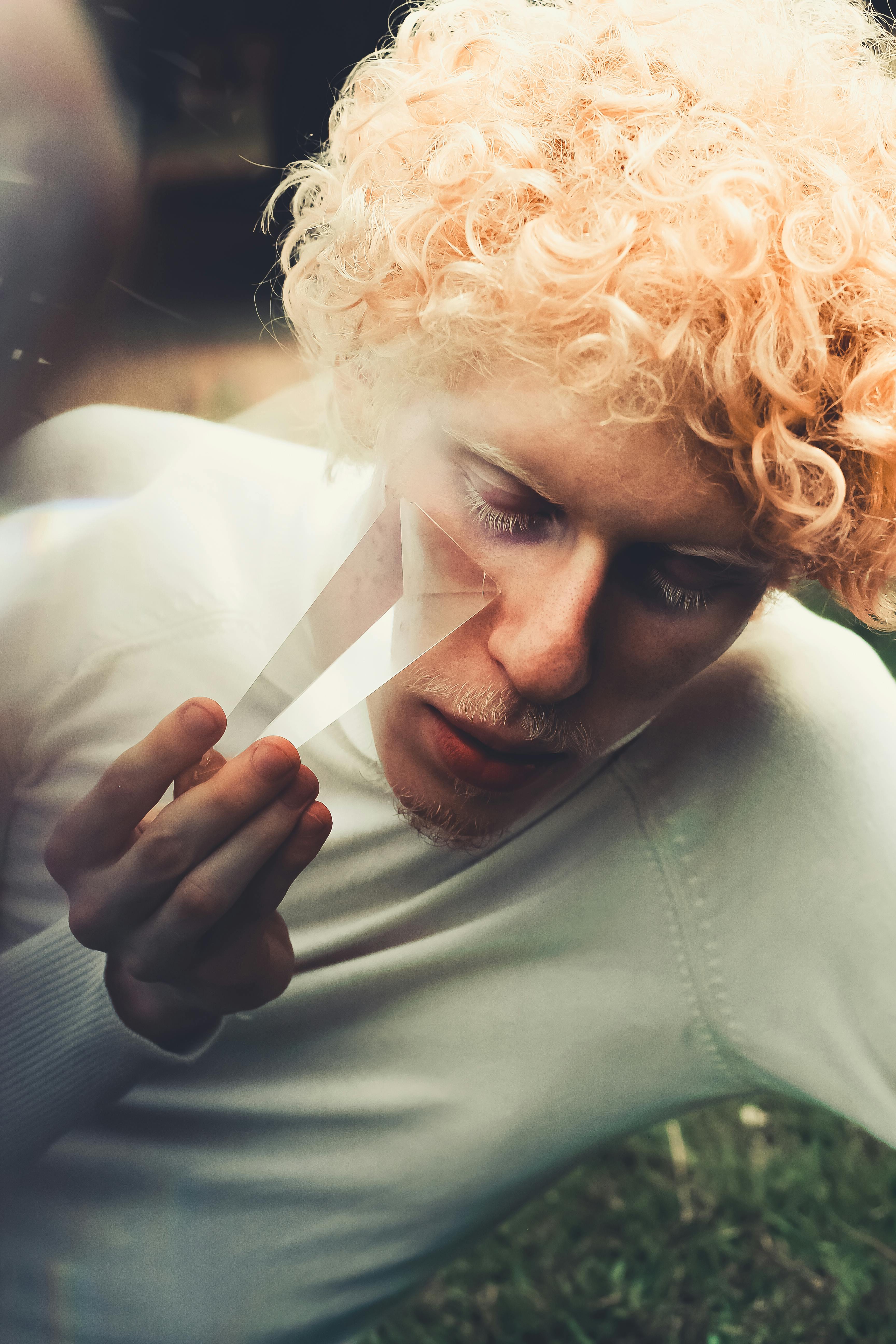 一个卷曲金发男人的特写肖像，在户外手持棱镜，创造出梦幻般的效果