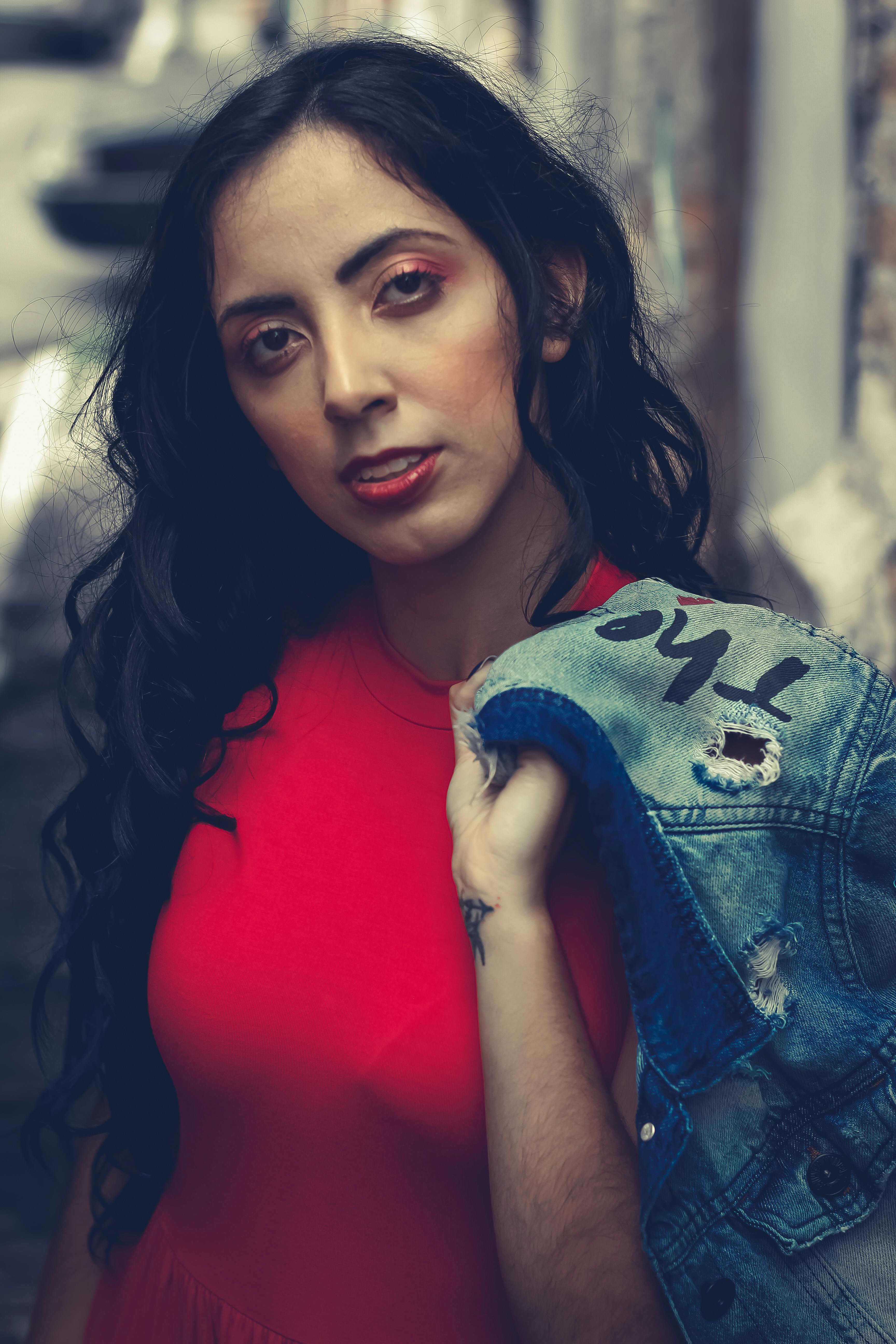 城市小巷中，一名身穿红色连衣裙、手拿牛仔夹克的女子特写肖像