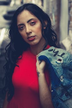 城市小巷中，一名身穿红色连衣裙、手拿牛仔夹克的女子特写肖像