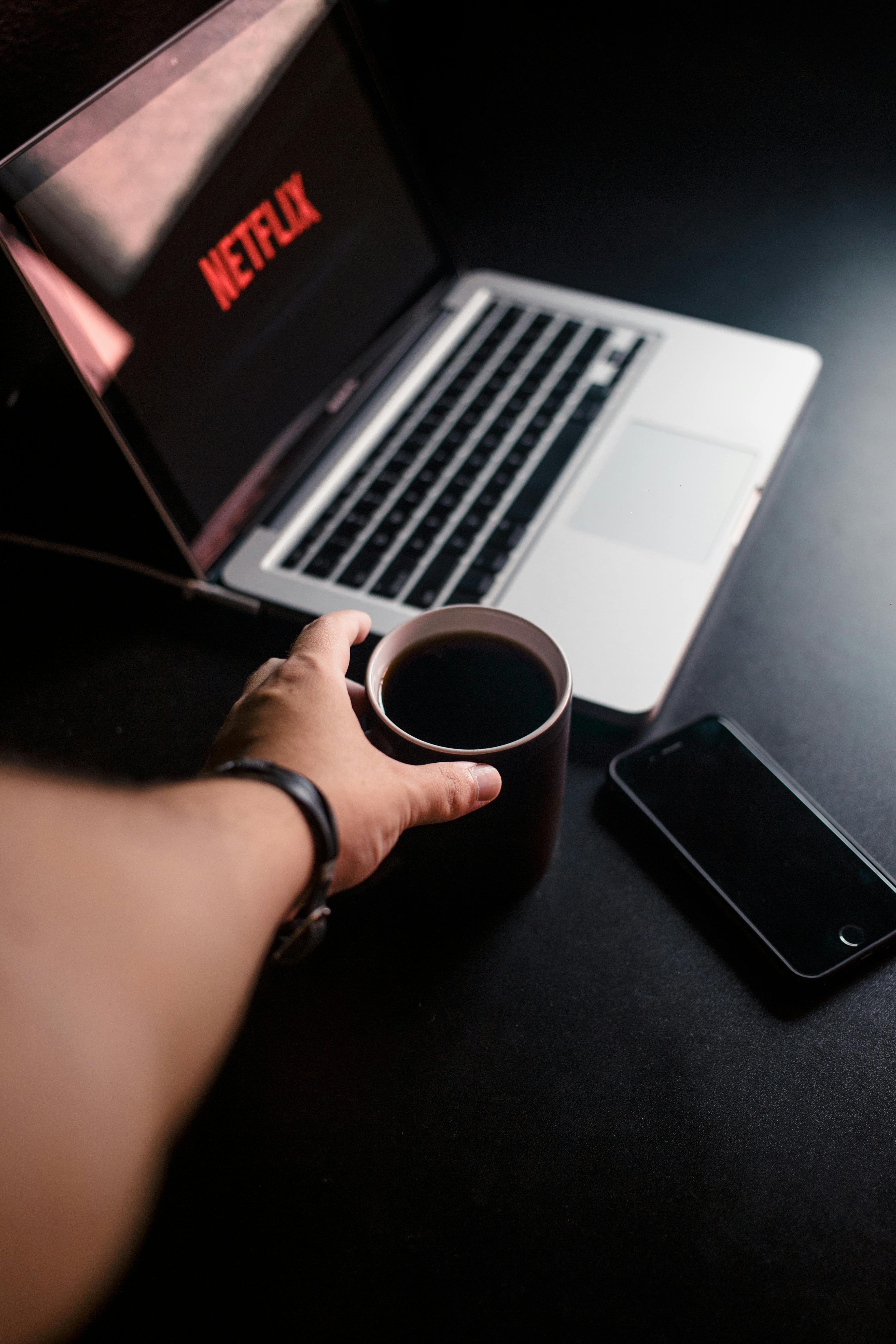 person reaching for mug with coffee near macbook pro and space gray iphone