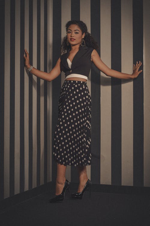 A woman in a polka skirt posing against a striped wall