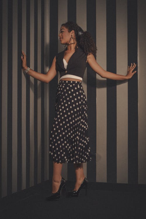 A woman in a polka dot skirt posing against a striped wall