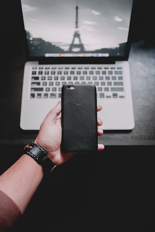 Free Person Holding Iphone Near Macbook Pro Stock Photo