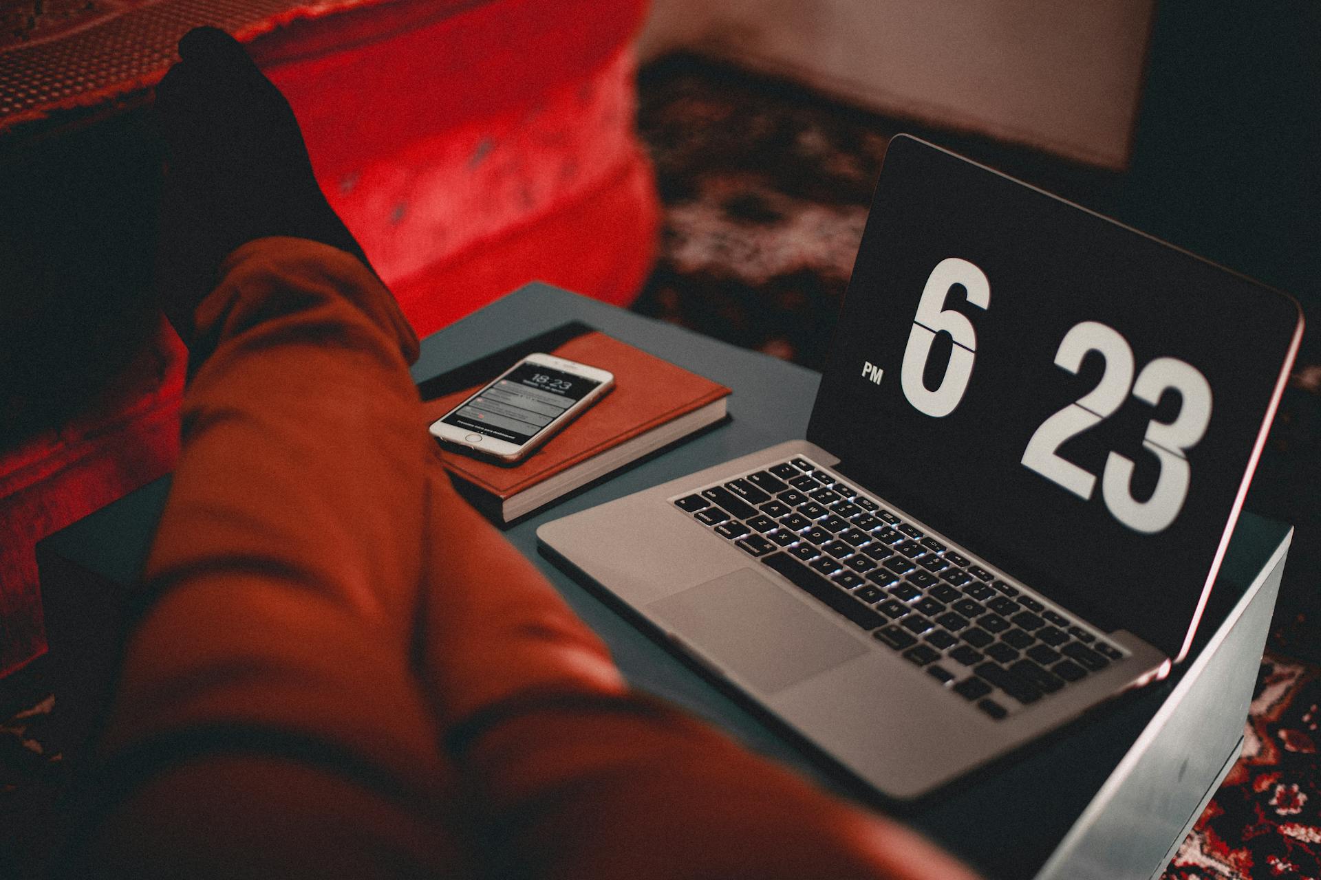 A relaxed indoor workspace features a laptop displaying time and a smartphone on a side table.