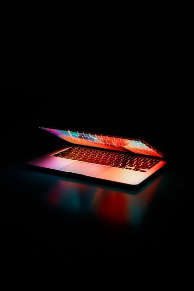 A laptop glowing on a desk in a dark office