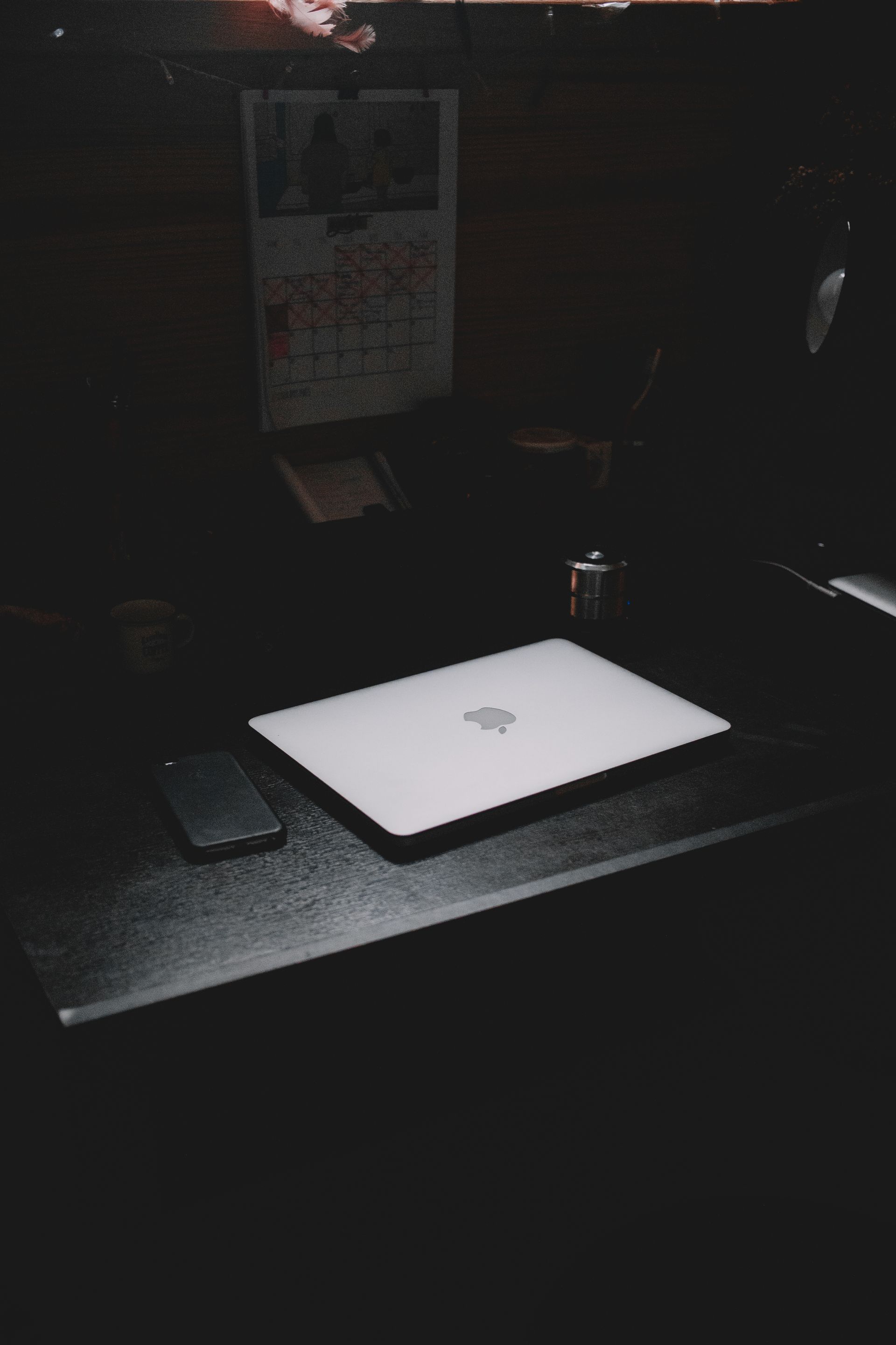 A dark, minimalist workspace featuring a laptop and smartphone on a desk